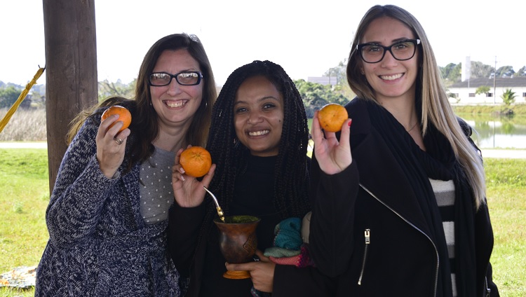 Três mulheres sorrindo mostrando as bergamotas em suas mãos