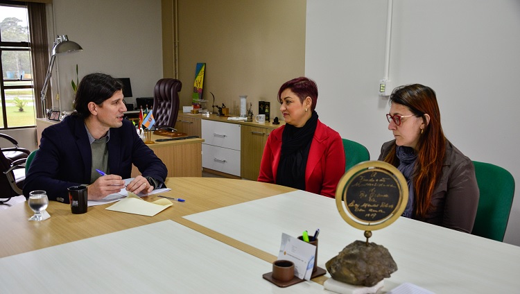 A foto mostra três pessoas sentadas à mesa conversando.