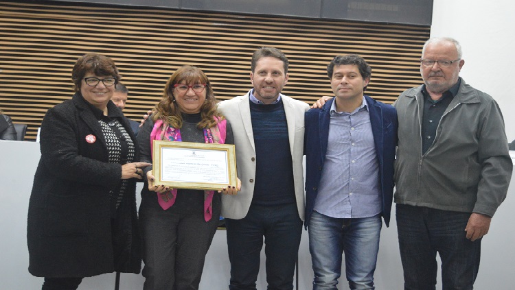 Cinco pessoas em pé seguram uma placa em homenagem ao aniversário do Caic