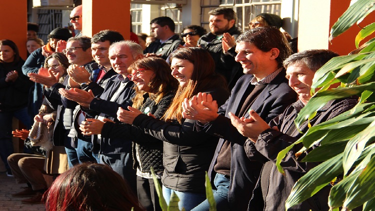 A imagem mostra grupo de pessoas na lateral da foto sorrindo e aplaudindo.