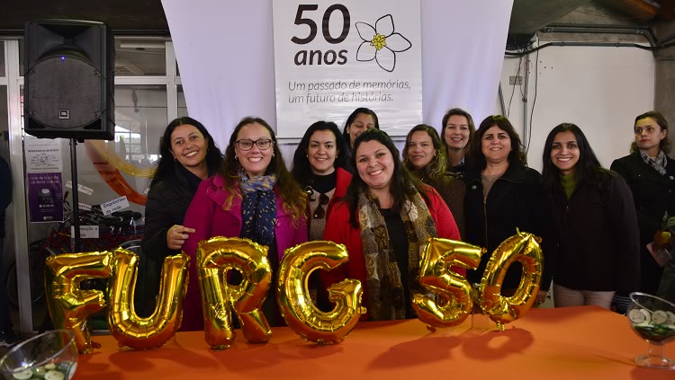 A imagem mostra pessoas na frente de uma mesa com balões comemorativos