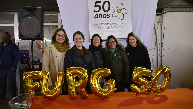 A imagem mostra pessoas na frente de uma mesa com balões comemorativos