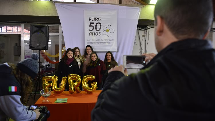 A imagem mostra pessoas na frente de uma mesa com balões comemorativos