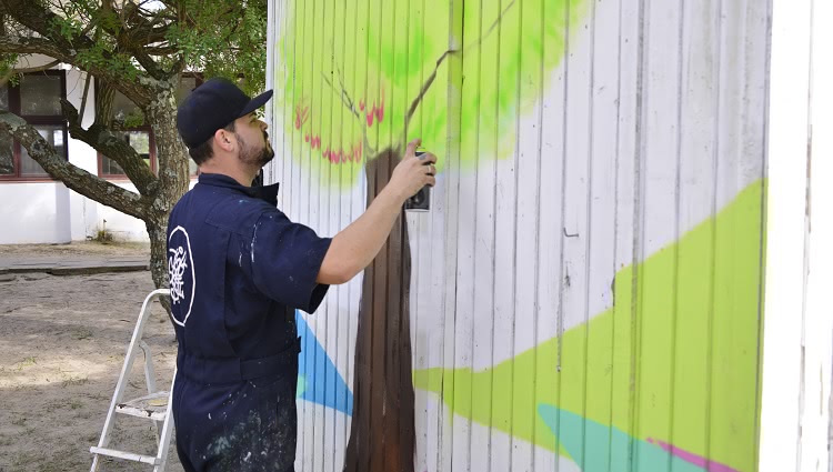 A imagem mostra uma pessoa grafitando uma parede