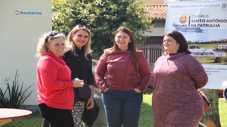 Na imagem mostra quatro mulheres em pé olhando em direção a foto.