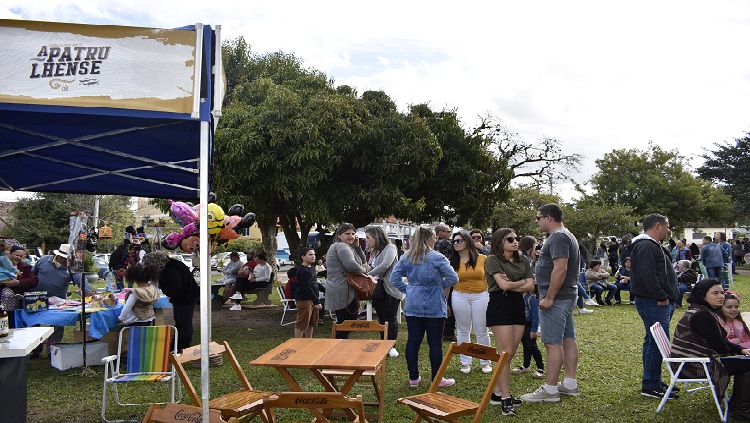 A imagem mostra pessoas em pé em meio as tendas de exposição na praça.