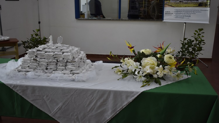 A imagem mostra uma mesa com diversos doces em cima, velas de aniversário e flores.