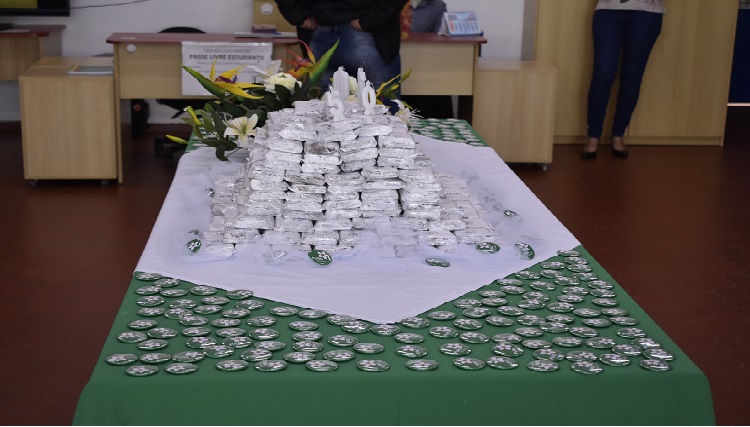 A imagem mostra uma mesa com doces, tolhas brancas e verdes e com diversos botons espalhados por cima da mesa,