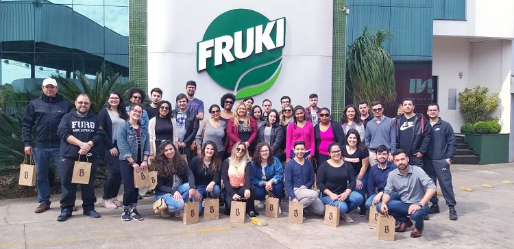 a imagem mostra os estudantes em grupo, em frente ao logo da empresa