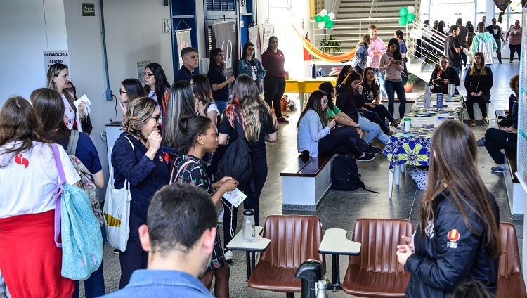 A imagem mostra o interior de um prédio da universidade, com muitas pessoas circulando. 