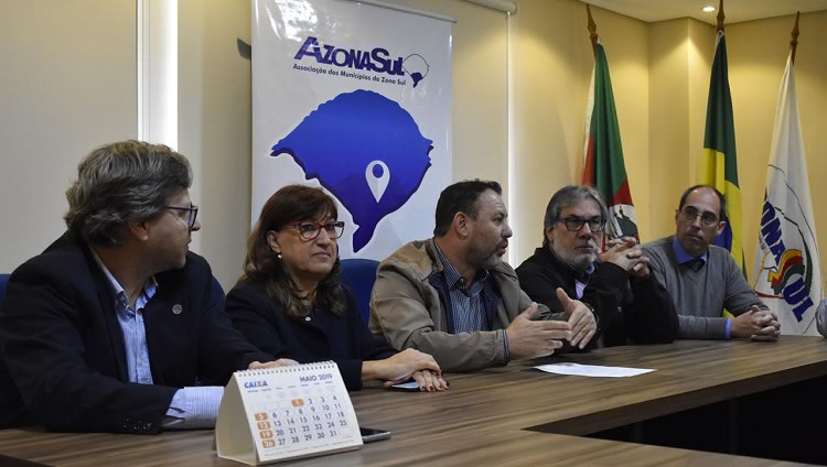 Em uma mesa, aparecem cinco pessoas, lado a lado. Da esquerda para a direita, a segunda pessoa é a reitora Cleuza Dias. Atrás deles, um banner em que se lê Azonasul