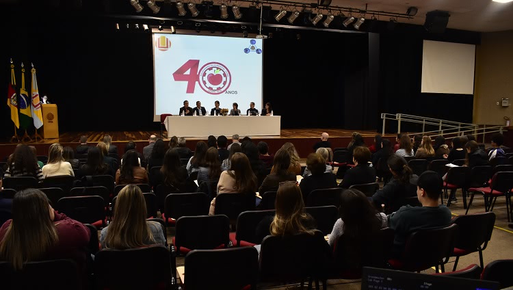 Imagem mostra cadeiras do auditório e, ao fundo, palco do evento