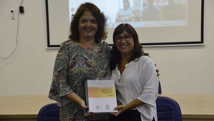 A imagem mostra a presidente da CPA Adriana Kivanski de Senna fazendo a entrega do Relatório de Avaliação Institucional 2018 para a reitora Cleuza Maria Sobral Dias