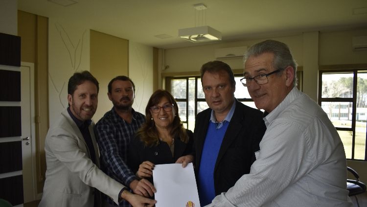 A imagem mostra cinco pessoas em pé olhando para foto mostrando documento assinado