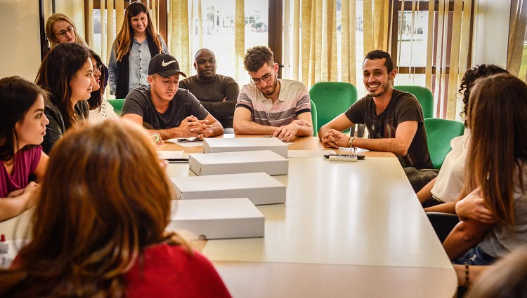 Imagem mostra estudantes internacionais ao redor de uma mesa