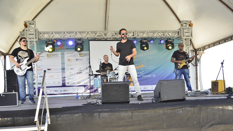 Na foto, uma banda com quatro músicos aparece tocando em um palco