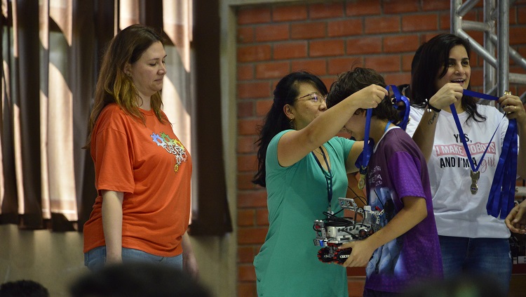 Uma mulher está colocando uma medalha em um menino, que segura um robô. 