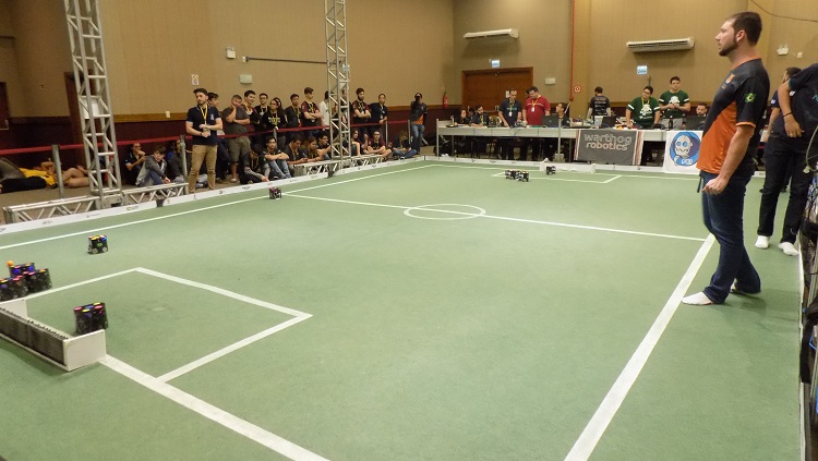 Na foto aparece um campo de futebol com vários pequenos robôs