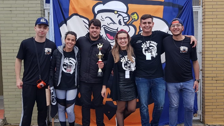 Seis pessoas posicionadas lado a lado, um deles segurando o troféu da competição