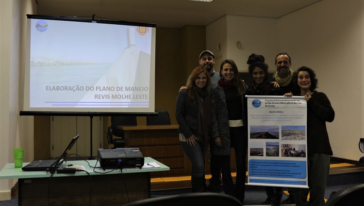 Em frente a uma projeção, a equipe de pesquisadores segura um cartaz com dados sobre o projeto 