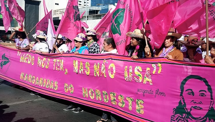 Mulheres segurando uma faixa escrita com uma frase de Margarida Alves 