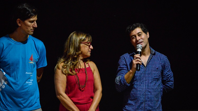 Três pessoas aparecem na foto, à frente de um fundo preto: à esquerda o vice-reitor Danilo, no centro a reitora Cleuza, e à direita, com o microfone à mão, o pró-reitor de extensão e cultura Daniel. 