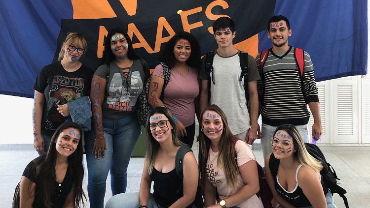 Estudantes posando para a foto em frente à uma bandeira da Associação Atlética do campus