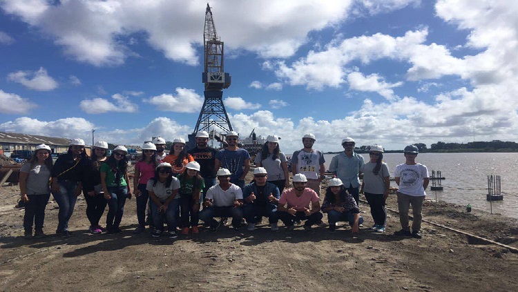 A imagem mostra grupo de pessoas em pé e outros agachados usando capacetes de proteção, nas obras do cais do Porto Velho